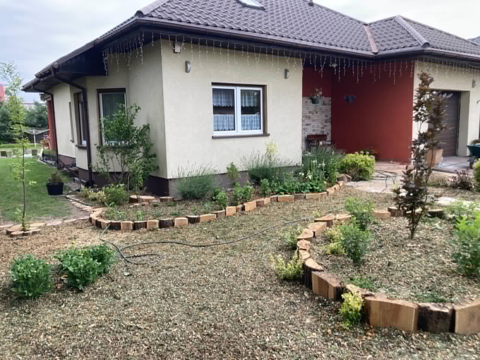 Ogród przydomowy z rabatami obrzeżonymi drewnem i nowymi nasadzeniami